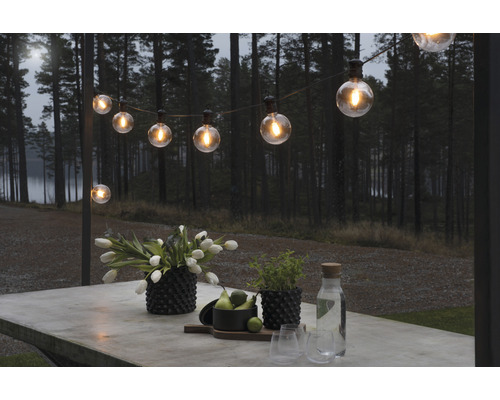 Belyst ljusslinga över ett bord utomhus med blommor, växter och drycker