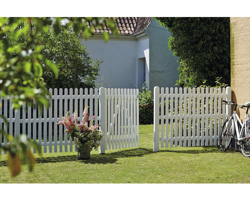 Scen med ett vitt staket och en öppen trädgårdsport på en gräsmatta