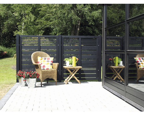 Trädgårdsscen med trästaket, rottingfåtölj, sidobord och blommor