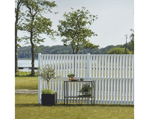 Miljöbild med vitt trädgårdsstaket, växter i krukor och ett trädgårdsbord