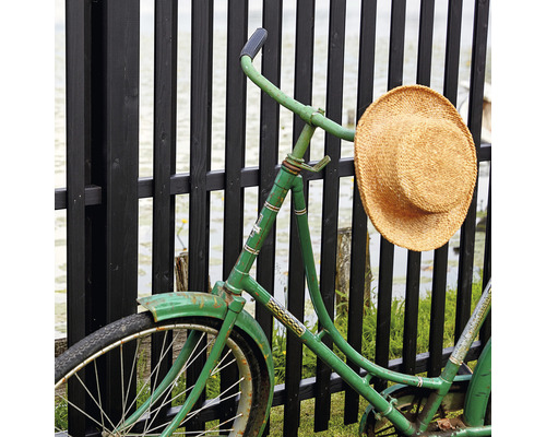 En grön cykel med en stråhatt på ett staket