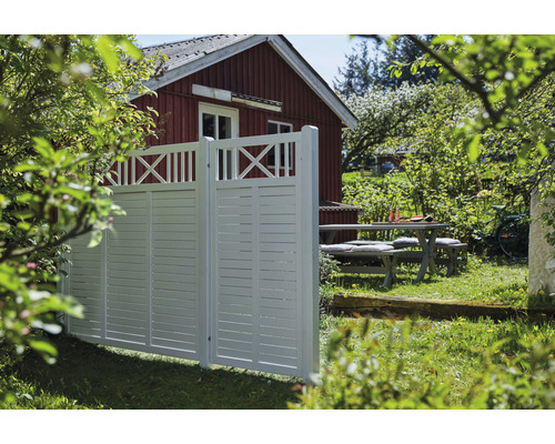 Vitt trädgårdsstaket med träbord och rött hus i bakgrunden