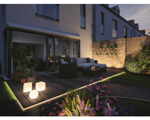 Upplyst terrass med trädgårdsmöbler, blomkrukor och dekorativ belysning.