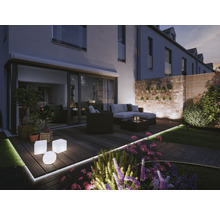Belyst trädgård med terrass, loungemöbler och blomsterrabatt