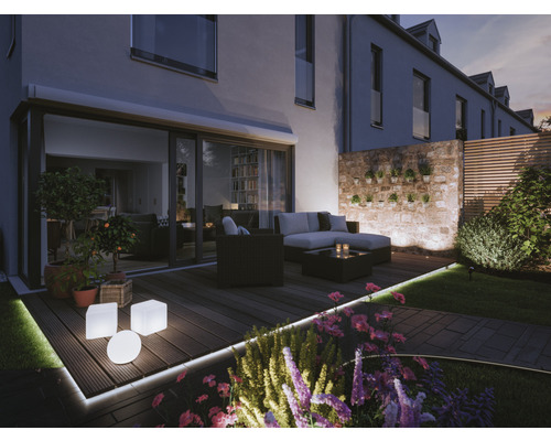 Belyst trädgård med terrass, loungemöbler och blomsterrabatt