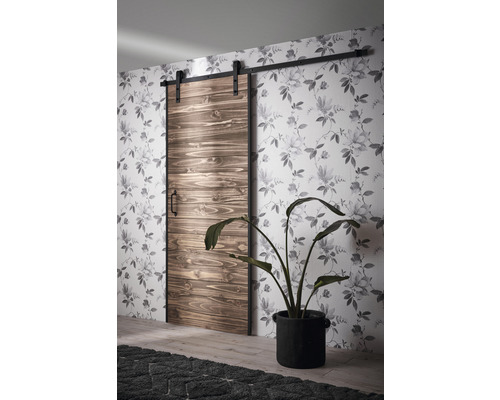 Skjutdörr i trä med beslag framför en vägg med blommönster