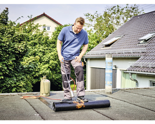 Hantverkare svetsar bitumenbana på ett platt tak med en brännare