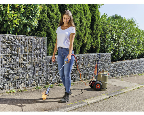 En kvinna använder en ogräsbrännare för ogräsbekämpning i trädgården.