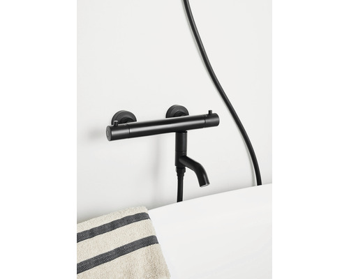 Svart utanpåliggande badkarsblandare på en vit vägg ovanför ett handfat