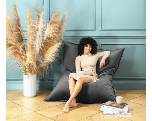 Kvinna sitter avslappnat på en grå sittsäck i ett rum med dekorativ blomvas