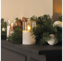 Dekorativt arrangemang med LED-ljus, grangrönt och ornament på en hylla.