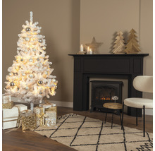 Konstgjord snötäckt julgran med bollar och presenter i ett vardagsrum med öppen spis