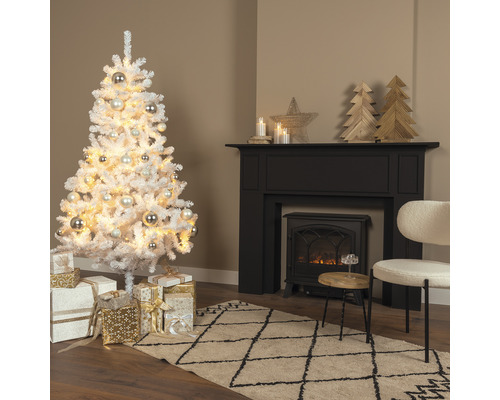 Konstgjord snötäckt julgran med bollar och presenter i ett vardagsrum med öppen spis