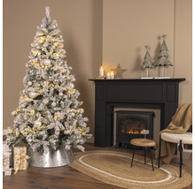 Festligt inrett rum med snötäckt julgran, öppen spis och dekorationer.