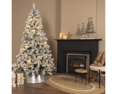 Festligt inrett rum med snötäckt julgran, öppen spis och dekorationer.