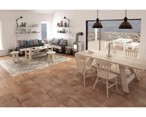 Vardagsrum med träbord, stolar, soffa, matta och eldstad på terrakotta klinker