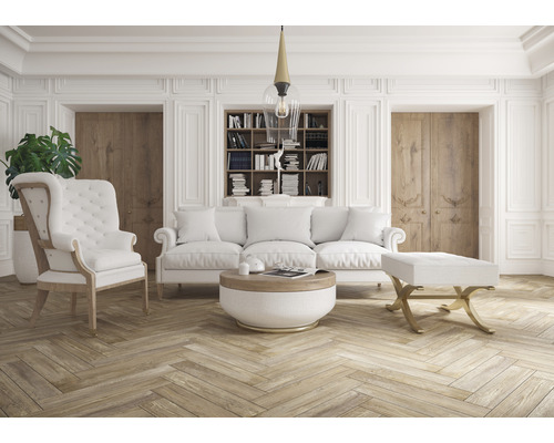 Vardagsrum med soffa, fåtölj, ottomaner, soffbord och bokhylla i ett ljust rum.