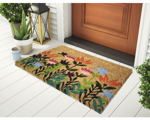 Dörrmatta av kokosfiber med blommönster framför en ytterdörr.