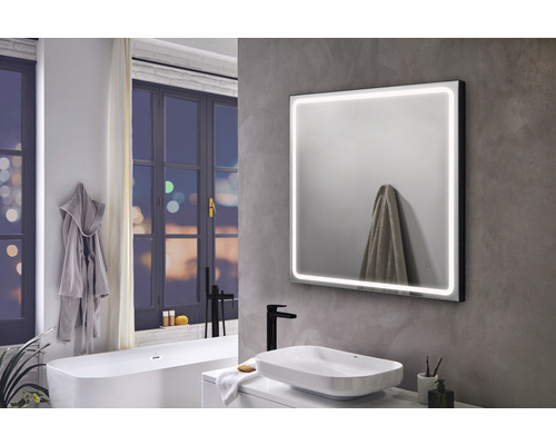 Modernt badrum med upplyst spegel, handfat och badkar under ett fönster