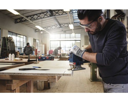 En man sågar ett arbetsstycke med en sticksåg i en verkstad.