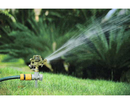 Grässpridare vattnar gräsmatta i trädgården.