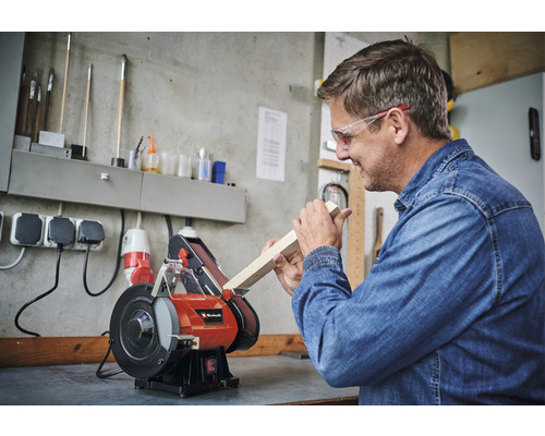 Man slipar träbit på en bandslipmaskin från Einhell i en verkstad.
