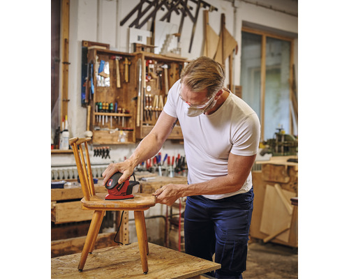 Man slipar en trästol med en excenterslipmaskin i en verkstad.
