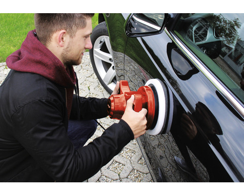 En man polerar en bil med en polermaskin.