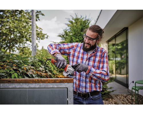 En man med skyddsglasögon slipar metall med en vinkelslip utomhus och gnistor uppstår.