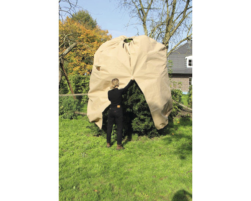 En kvinna täcker en buske i trädgården med en växtskyddshuva.