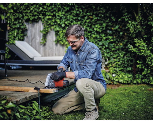 En man arbetar med en handsåg i trädgården och skär trä.