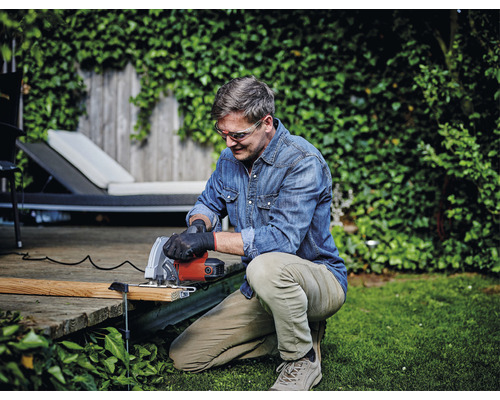 En man arbetar i trädgården med en handsåg och bär skyddsglasögon.