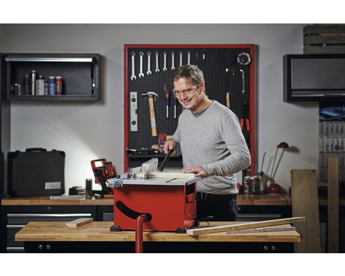 Man arbetar med en bordsågcirkelsåg i en verkstad. I bakgrunden finns verktyg och verkstadsutrustning.