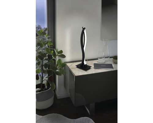 Dekorativ LED-bordslampa på ett nattduksbord bredvid en krukväxt.