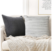 Två dekorativa kuddar med en stickad pläd på en soffa.