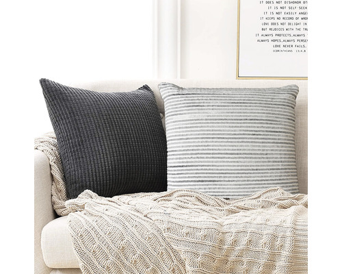 Två dekorativa kuddar med en stickad pläd på en soffa.