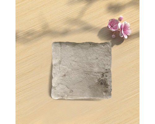 Fyrkantig, beige prydnadskudde med pälsstruktur på ljus träbakgrund