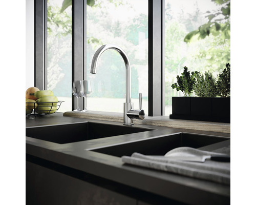 Köksscen med diskbänksblandare, diskho, frukt och örter framför ett fönster