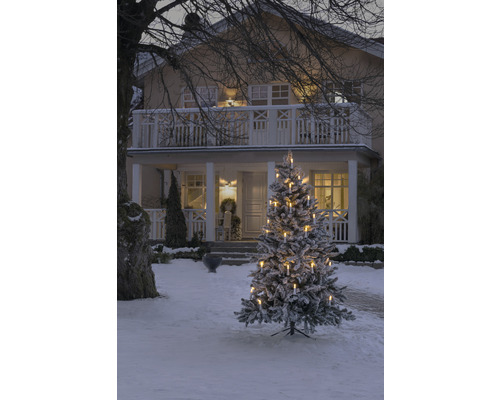 Snöig julgran med ljus framför ett hus på vintern