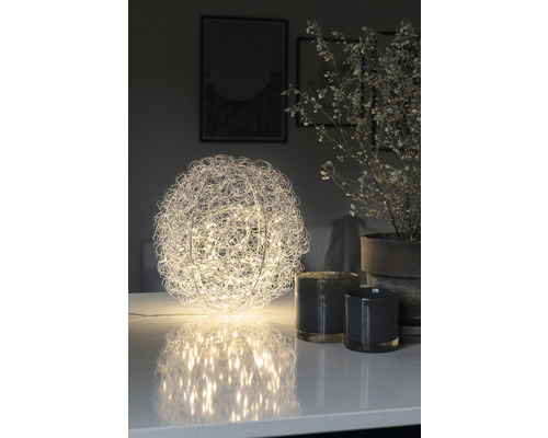 Dekorativ bordslampa i klotform med metalltrådsnät och LED-lampor på ett bord