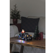 Dekorativ julscen med jultomten i en veteranbil, belyst, på ett träbord.