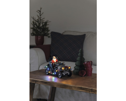 Dekorativ julscen med jultomten i en veteranbil, belyst, på ett träbord.