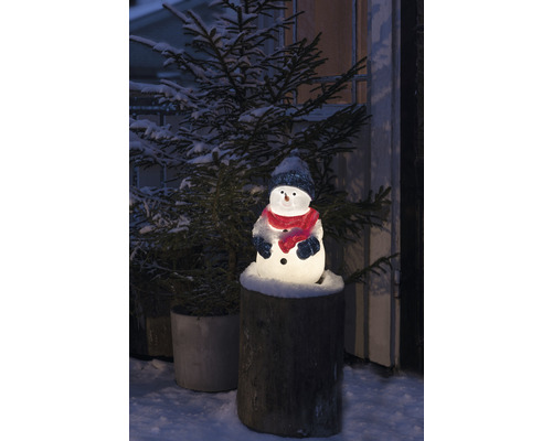 Lysande snögubbe med hatt och halsduk på en trädstubbe, omgiven av en snötäckt julgran.