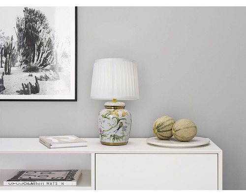 Dekorativ bordslampa med blommönster på en byrå med meloner och en fotoram