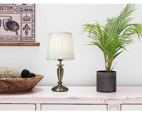 Dekorativ bordslampa bredvid krukväxt och skål med frukt på byrå