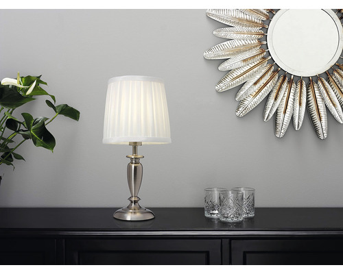 Dekorativ scen med bordslampa, spegel och glas på en byrå.