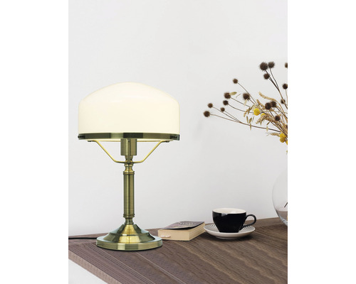 Bordslampa med glasskärm på ett bord med bok och kopp