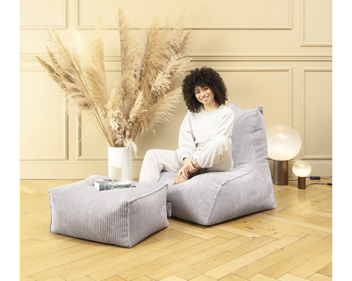 Kvinna sitter på en grå manchester-sittsäck med matchande pall i ett ljust rum.