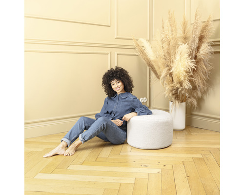 Kvinna sitter på en rund, vit pall i ett rum med trägolv