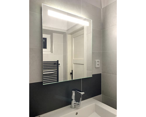 Badrum med spegel inklusive belysning ovanför ett handfat med kran